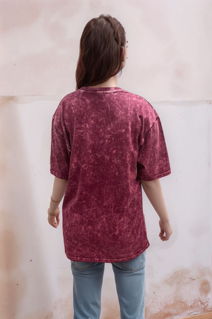 Person wearing a maroon acid wash shirt and light blue jeans against a textured wall.