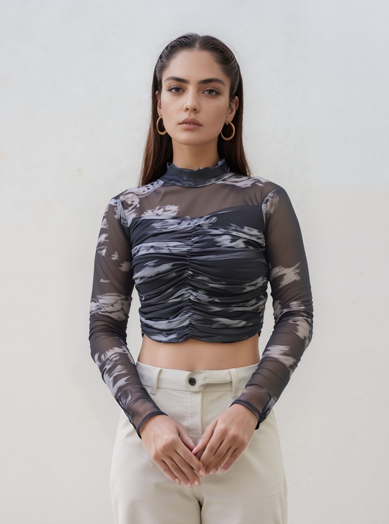 Model wearing black and grey marble swirl mesh ruched crop top with high neckline and sheer long sleeves, styled with high-waisted  jeans