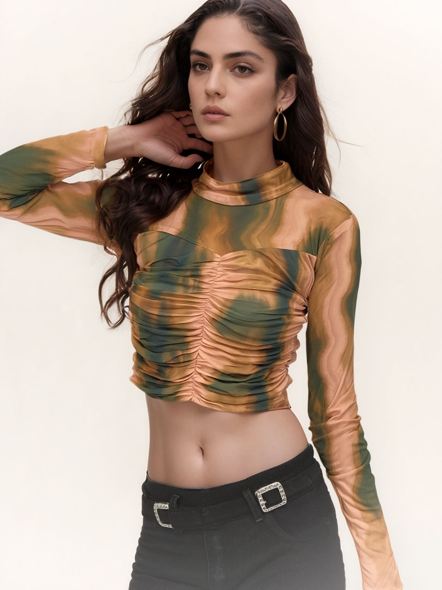 Model wearing a ruched mesh crop top with swirl marble pattern in green, mustard yellow, and brown shades, featuring full sleeves and a high neckline