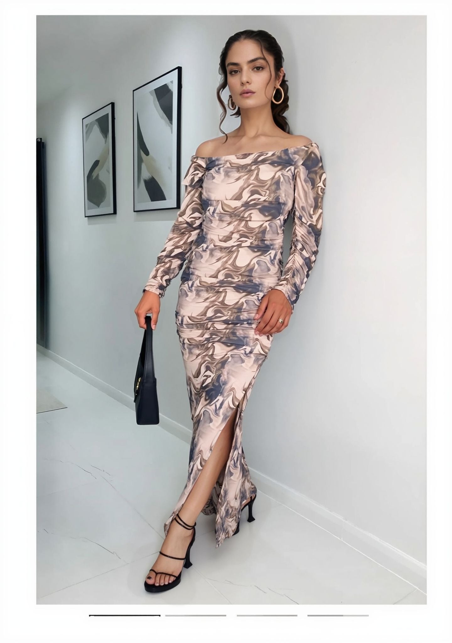 Woman posing in marble print off-shoulder maxi dress with side slit, paired with heels and handbag.
