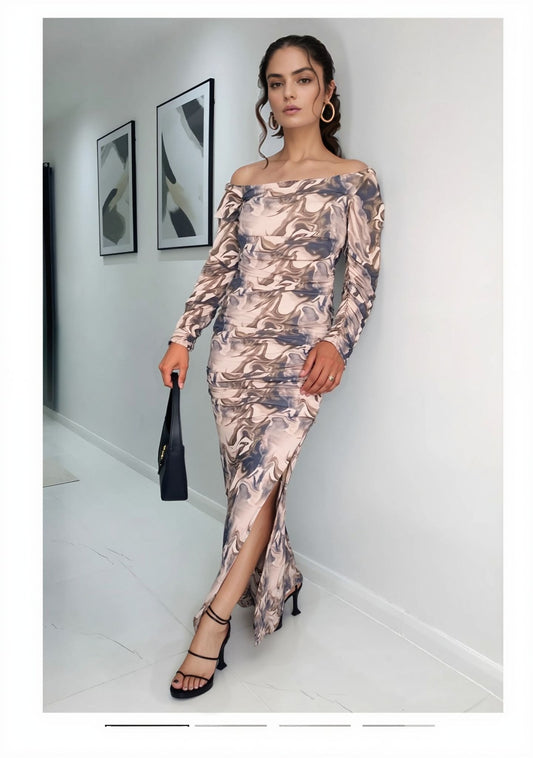 Woman posing in marble print off-shoulder maxi dress with side slit, paired with heels and handbag.