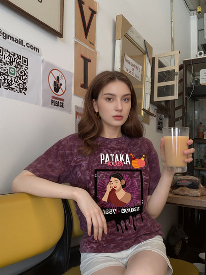 Woman wearing a maroon t-shirt with a graphic design, sitting in a room with various decorations.