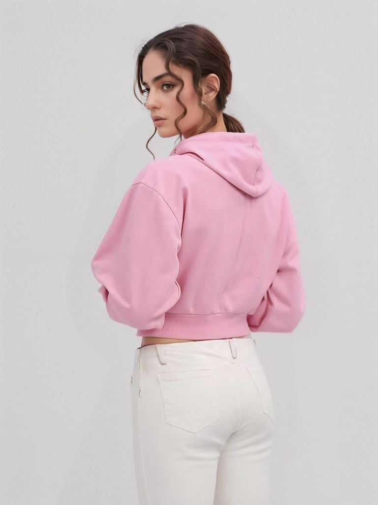 Back view of a pink cropped hoodie worn by a woman in white high-rise jeans, showing the hoodie’s fit and hem detail.