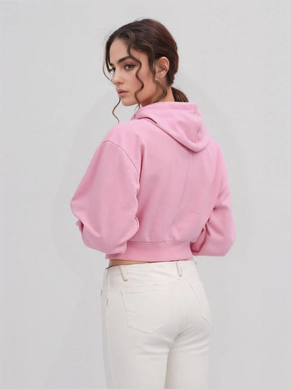 Back view of a pink cropped hoodie worn by a woman in white high-rise jeans, showing the hoodie’s fit and hem detail.