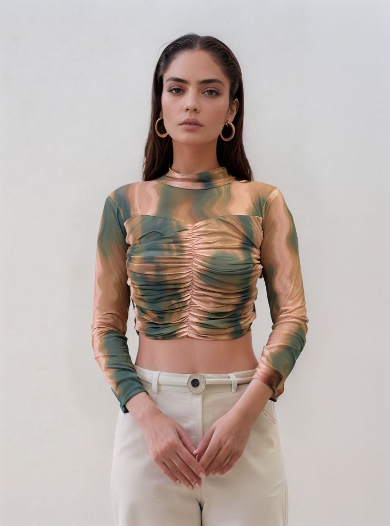 Model wearing green, mustard yellow, and beige swirl print ruched mesh crop top with high neckline and full sleeves, paired with white high-waist pants.