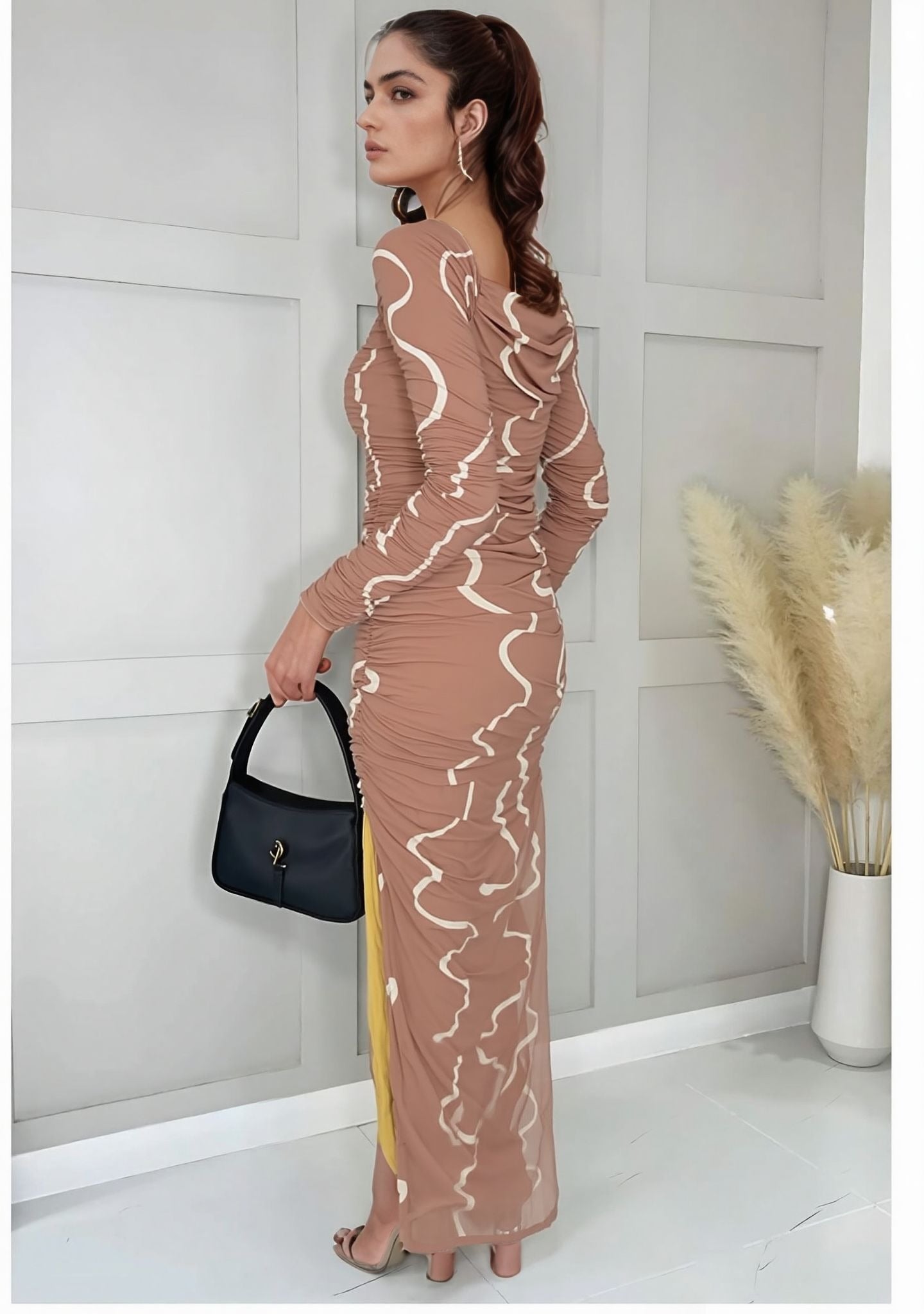 Side view of model in swirl print ruched dress, accessorized with black handbag and hoop earrings
