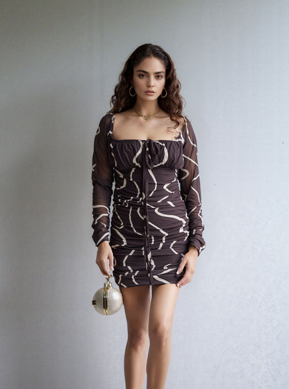 Woman wearing a patterned dress holding a metallic bag against a plain background