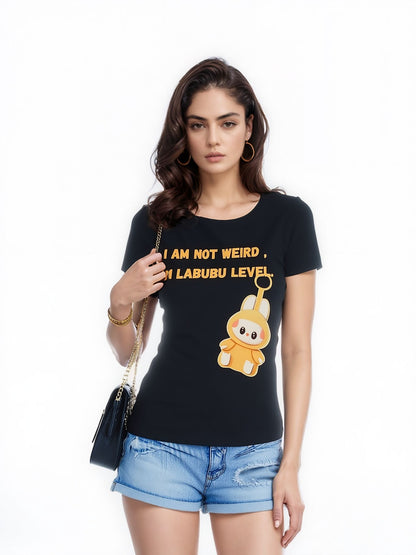 A woman wearing a black t-shirt with the text "I AM NOT WEIRD, I'M LABUBU LEVEL" and a cartoon character printed on it, paired with distressed denim shorts and a black shoulder bag, standing against a white background.

