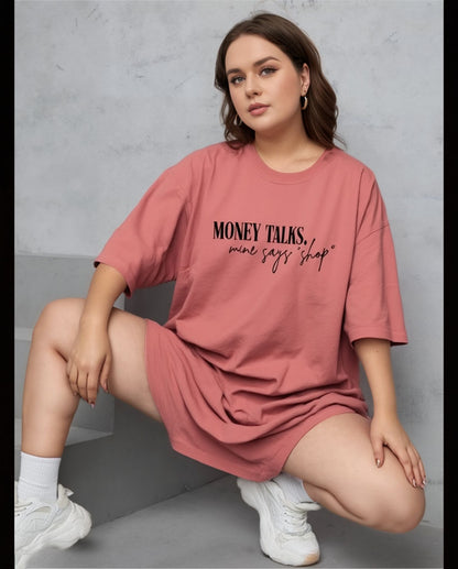 Woman wearing a pink oversized t-shirt with text, sitting on a gray surface.
