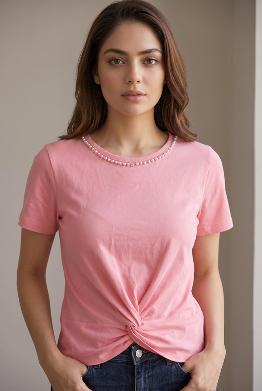 Front portrait pose of a woman wearing a blush pink pearl embellished twist top paired with dark blue denim and hands in pockets.