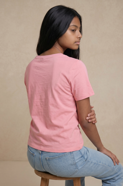 Back sitting pose of a woman wearing a blush pink cotton twist top with a pearl embellished neckline and light blue jeans.
