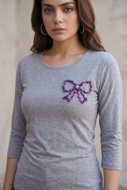 Woman wearing a grey full sleeve cotton T-shirt featuring a hand-embellished purple pearl bow design.
