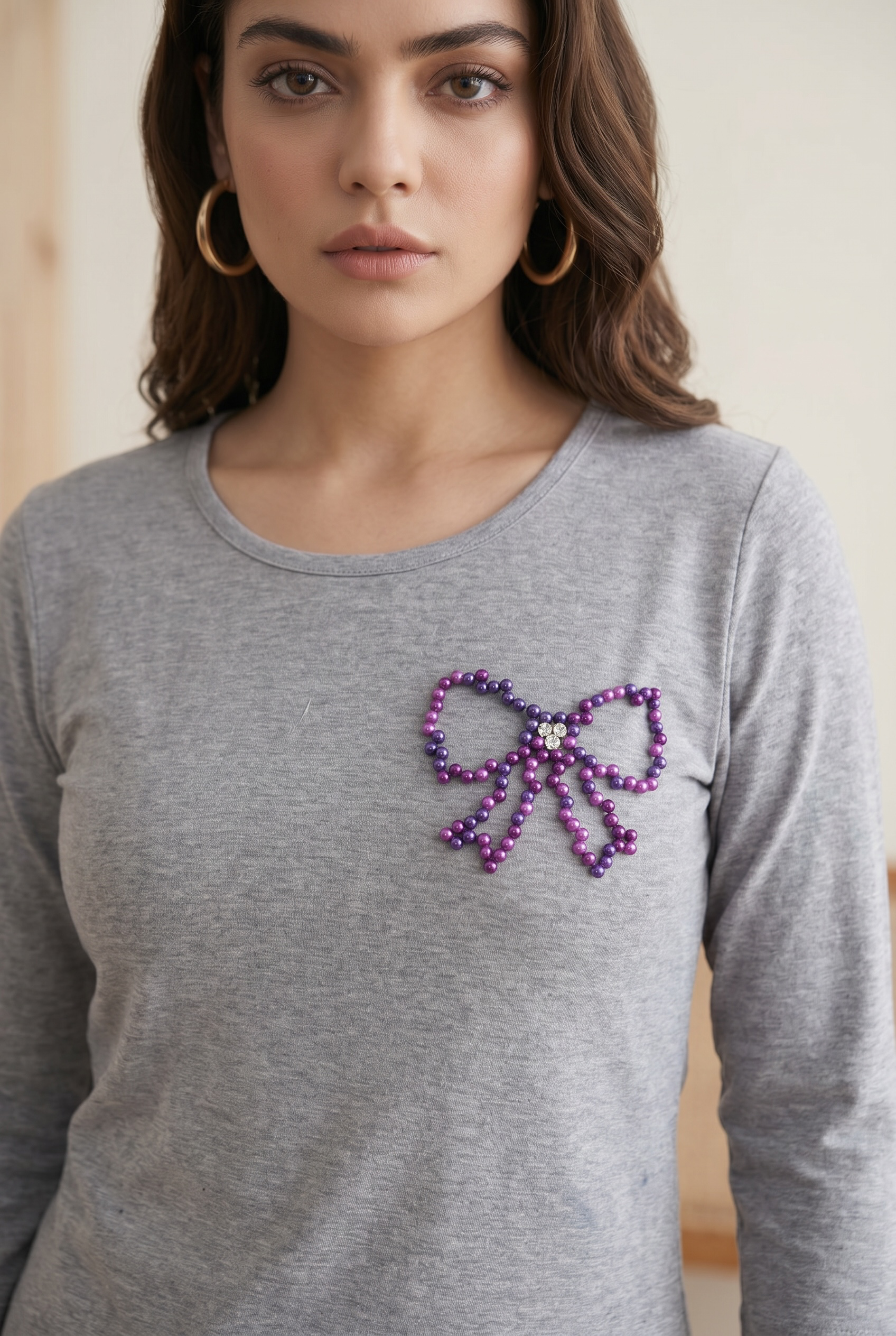 Close-up of women’s grey round neck full sleeve T-shirt with purple pearl bow embellishment.
