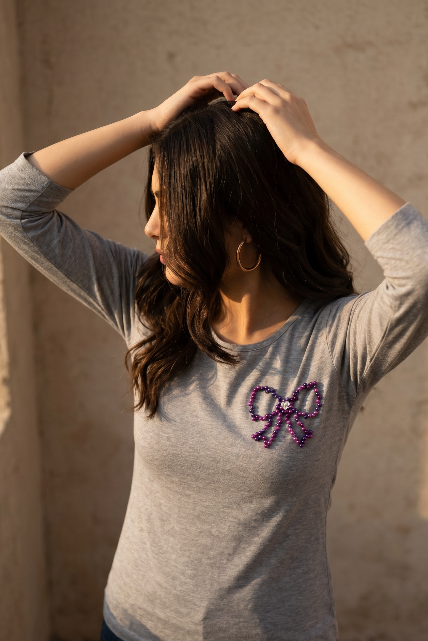 Lifestyle image of a woman wearing a grey full sleeve cotton T-shirt with an embellished pearl bow detail.