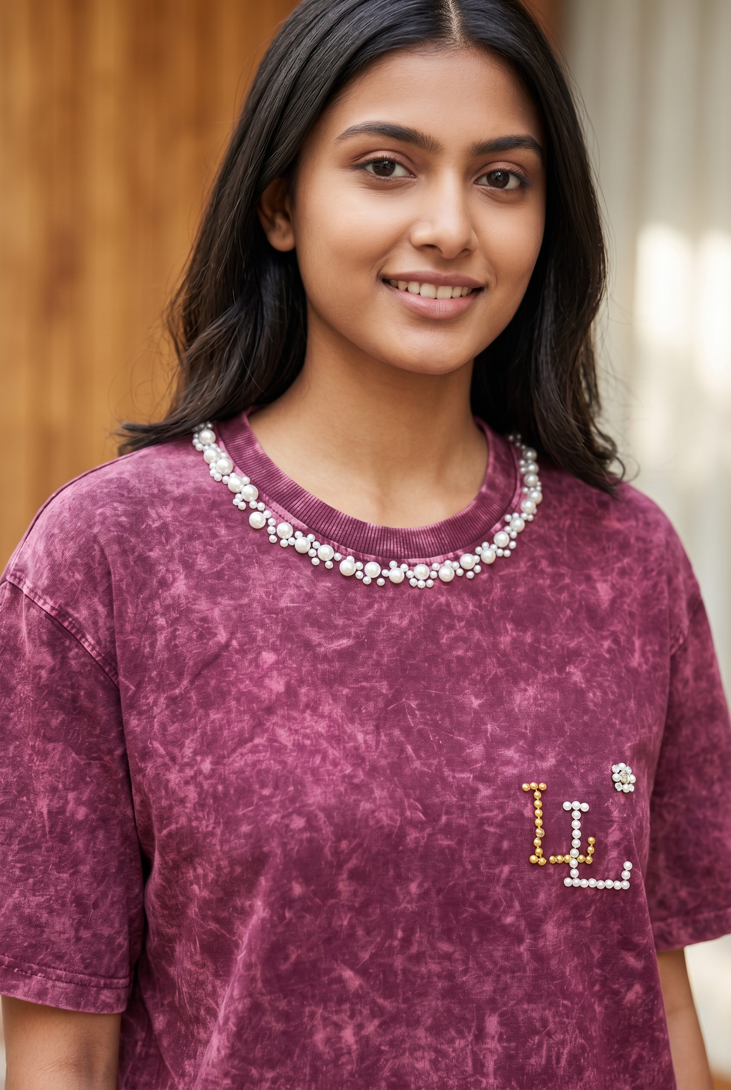 Close-up of maroon acid wash oversized T-shirt featuring pearl neckline and handcrafted pearl logo detailing.
