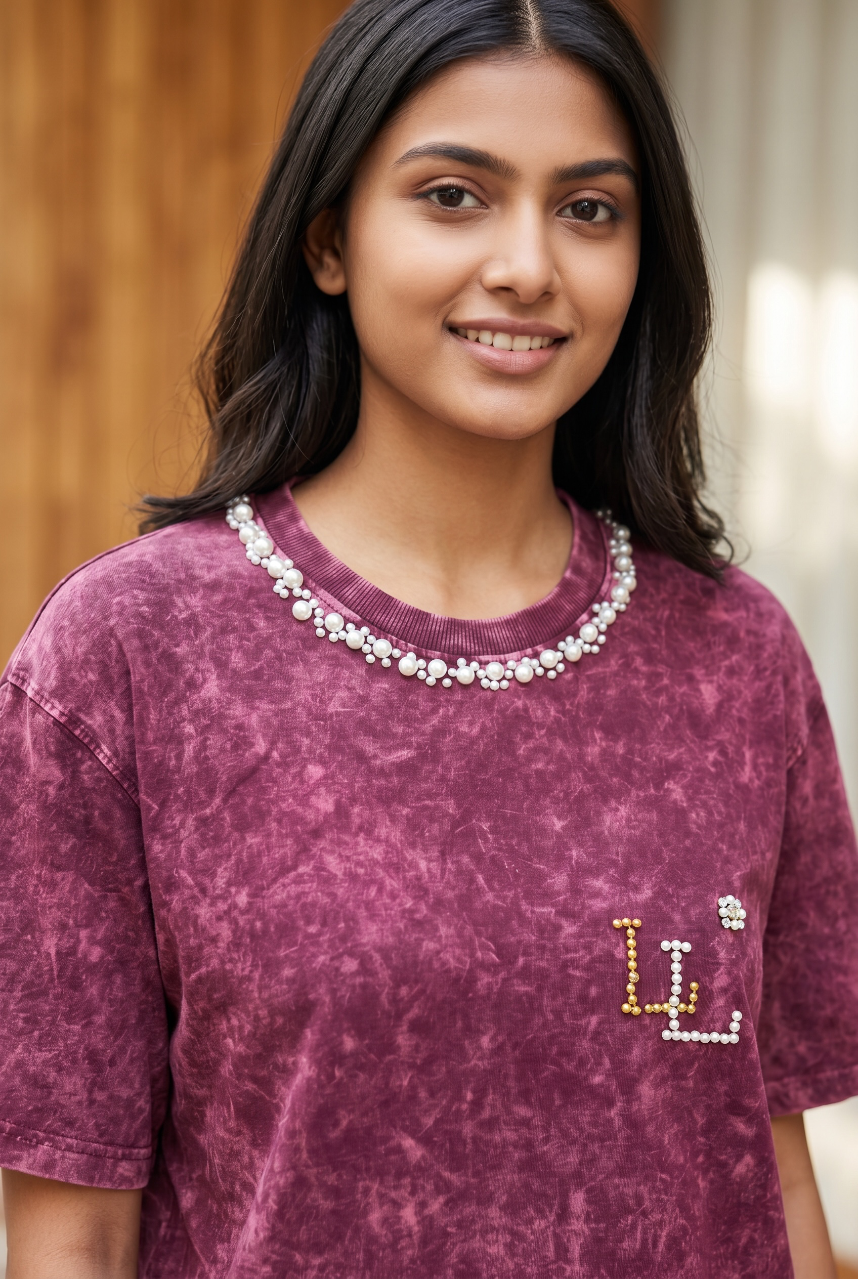 Close-up of maroon acid wash oversized T-shirt featuring pearl neckline and handcrafted pearl logo detailing.

